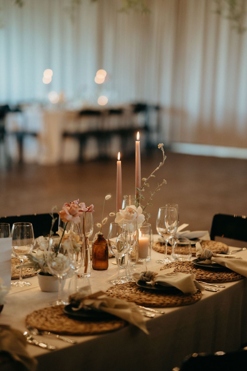 Romantic wedding table setting with glowing candles, amber bottles, and elegant place settings on white tablecloth.
