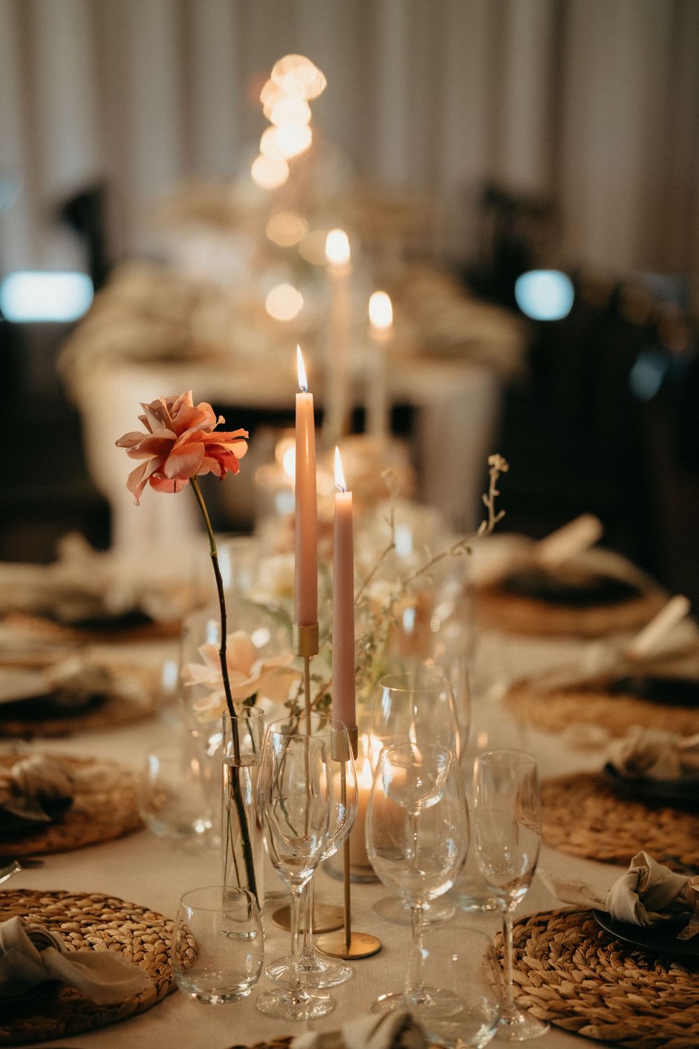 Elegant wedding table setting with taper candles, coral flowers, and woven charger plates.