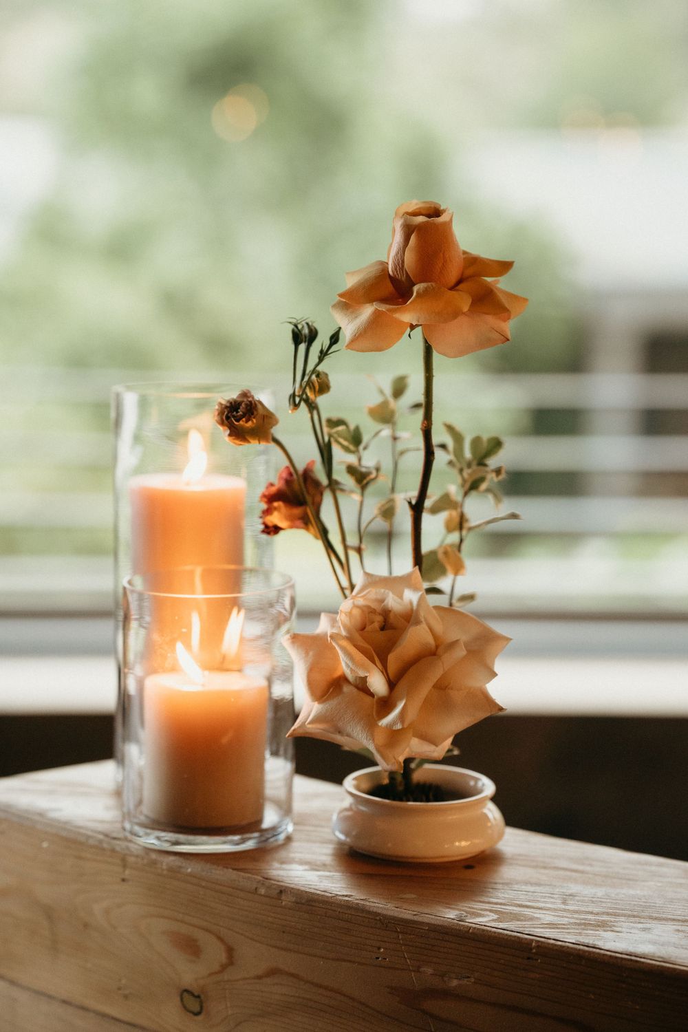 Peaceful wedding decor with glowing candles and peach roses arranged on wooden surface by window.