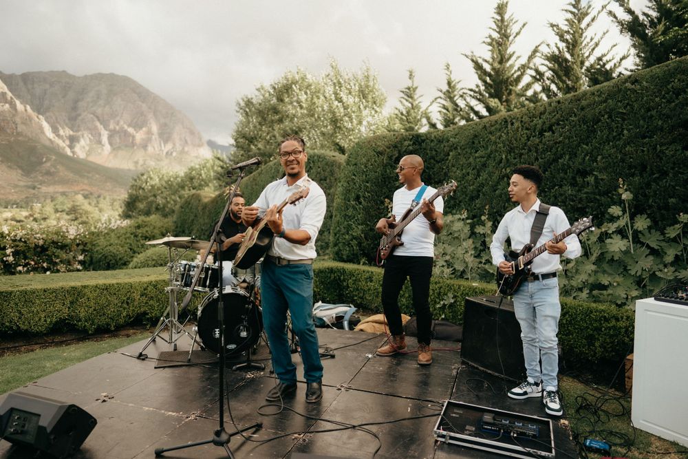 Live band performing at an outdoor wedding venue with mountain landscape in background.