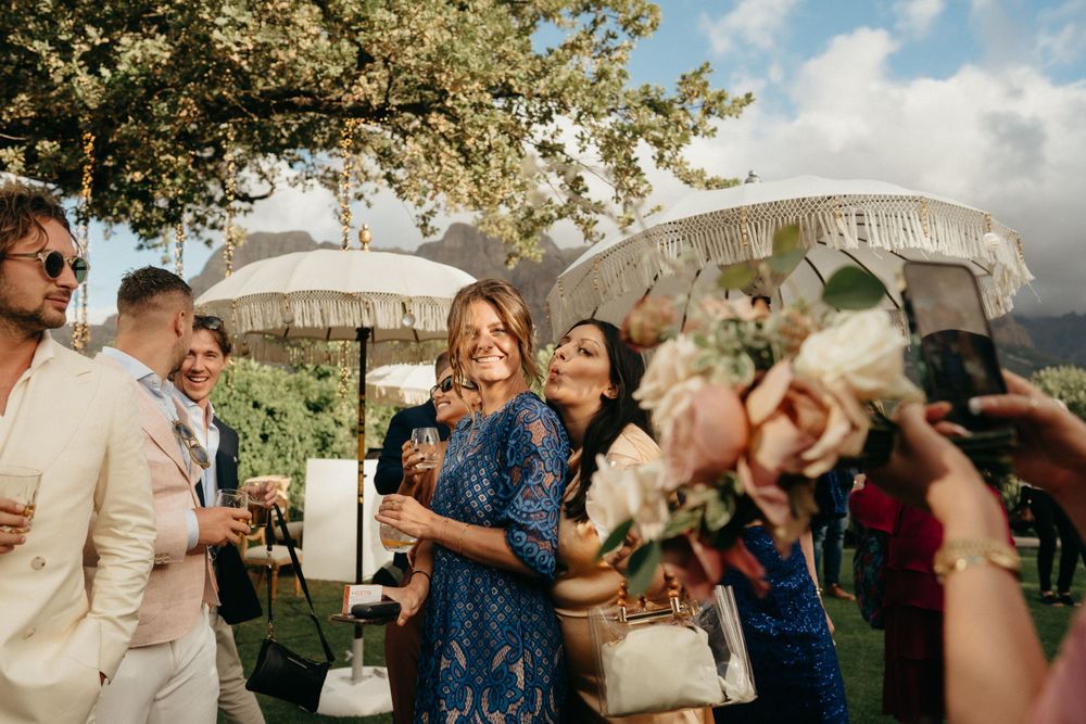 Outdoor wedding reception guests mingle under white parasols on a sunny afternoon.