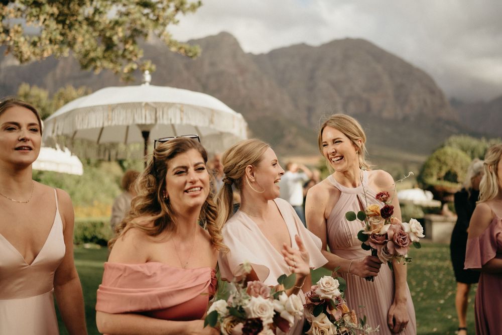 Wedding party in pink dresses holding parasols against dramatic mountain backdrop.