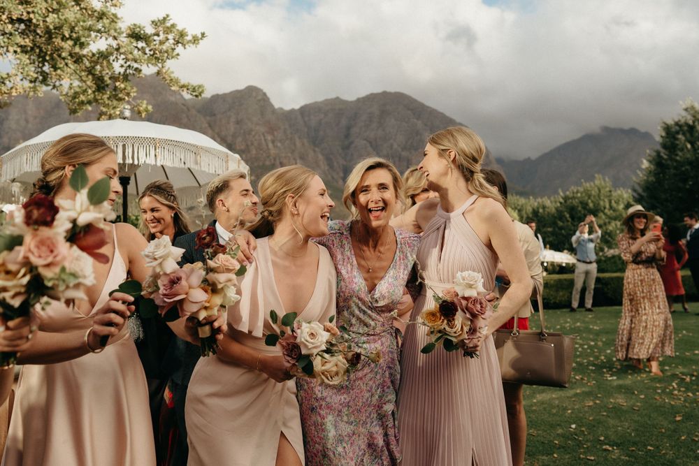 Wedding party enjoying candid moments together with scenic mountains in backdrop at outdoor celebration.