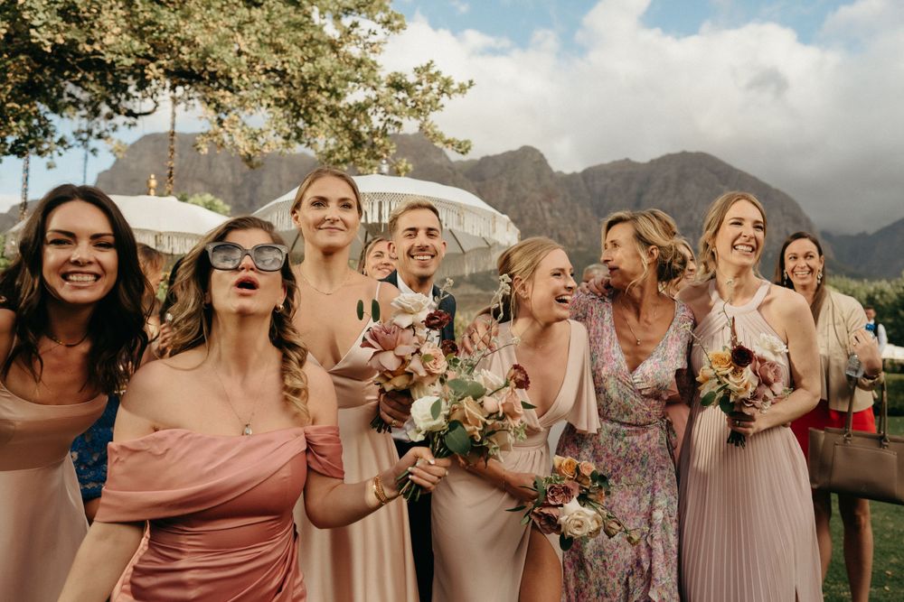Wedding party in blush and pink dresses celebrating outdoors with mountain scenery in the background.