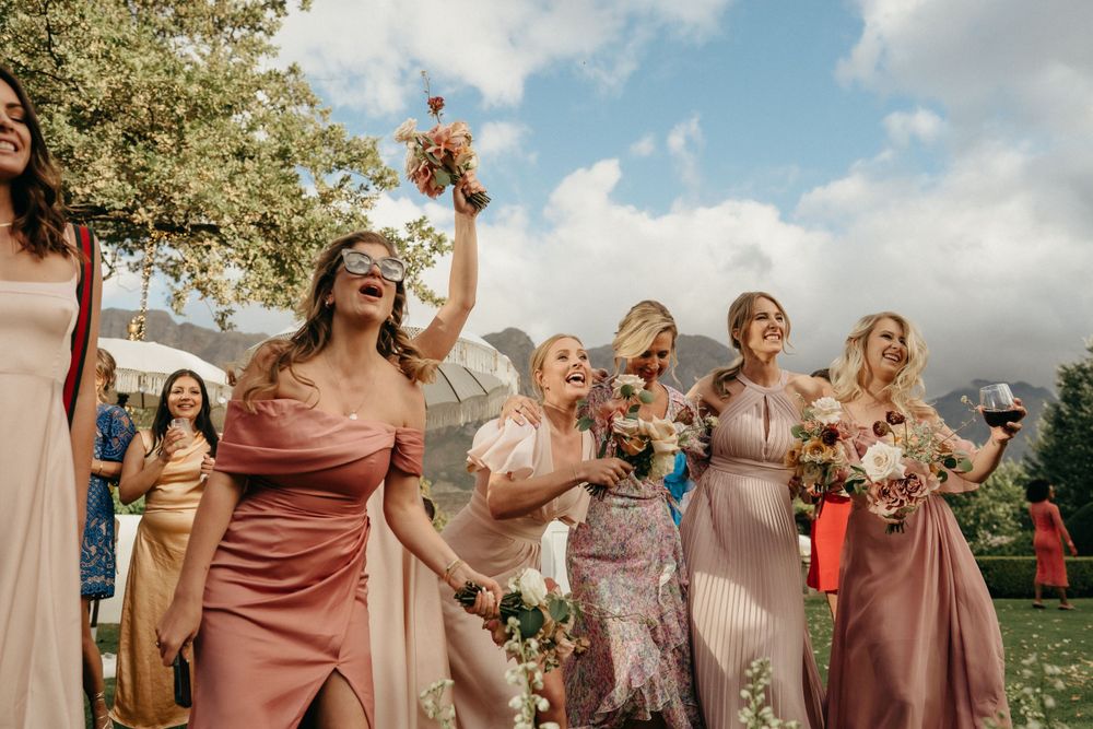 Wedding party celebrating outdoors with bouquets against mountain backdrop.