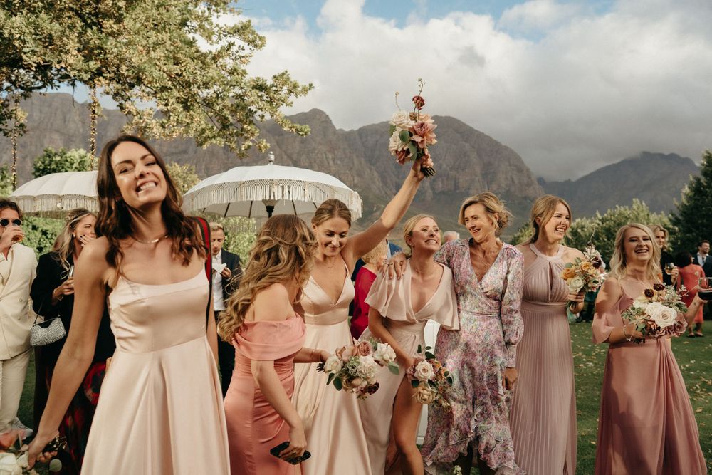 Joyful wedding celebration with guests in pastel dresses against a mountain backdrop.