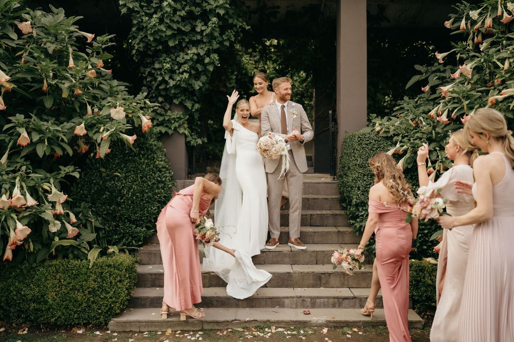 Wedding party helps with the bride's dress on stone steps surrounded by lush greenery.