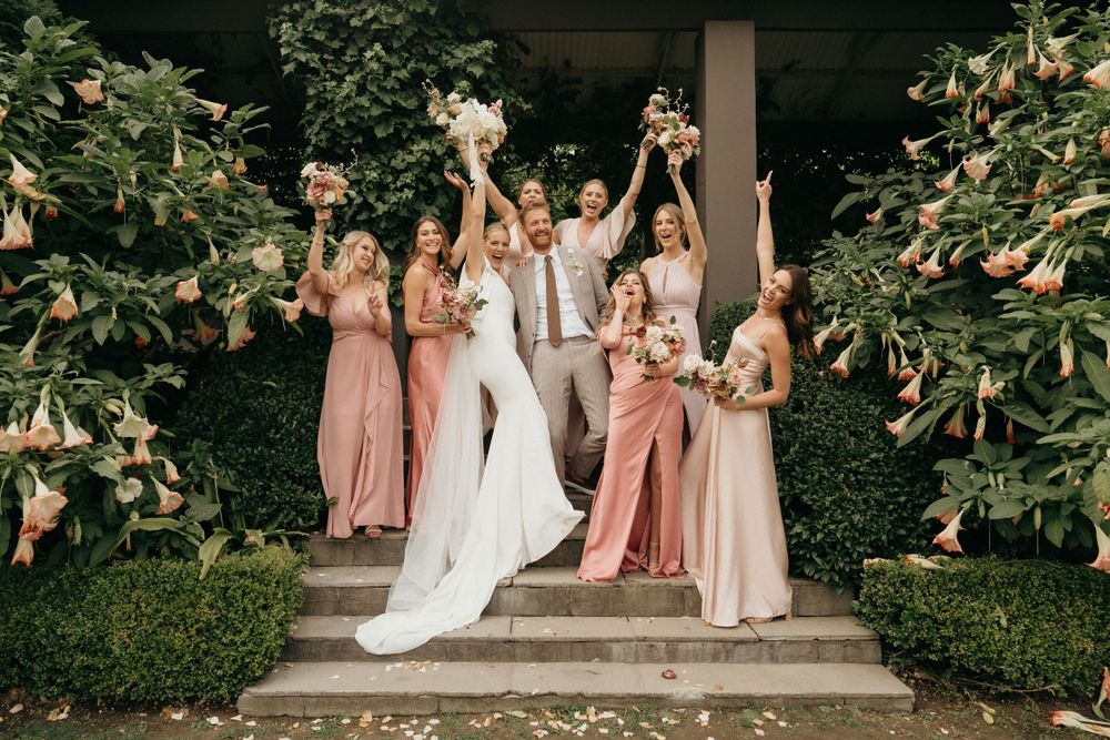 Wedding party celebrating on stone steps surrounded by magnolia trees.