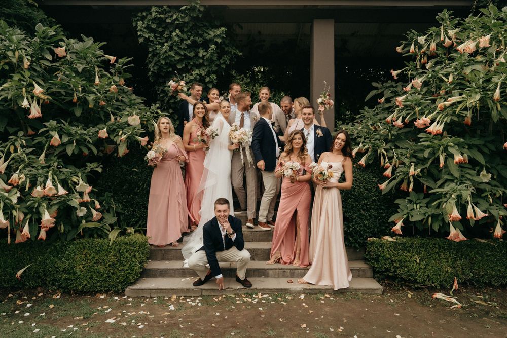 Wedding party gathered on steps surrounded by floral arrangements in pink tones.