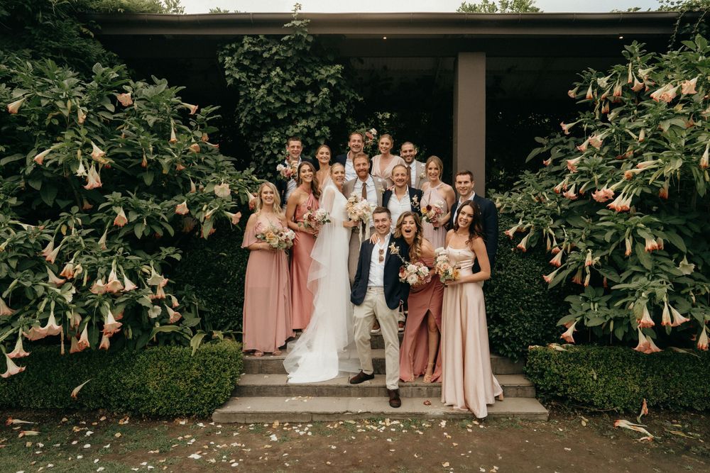 Wedding party in pink dresses poses together on stone steps for formal group photo.