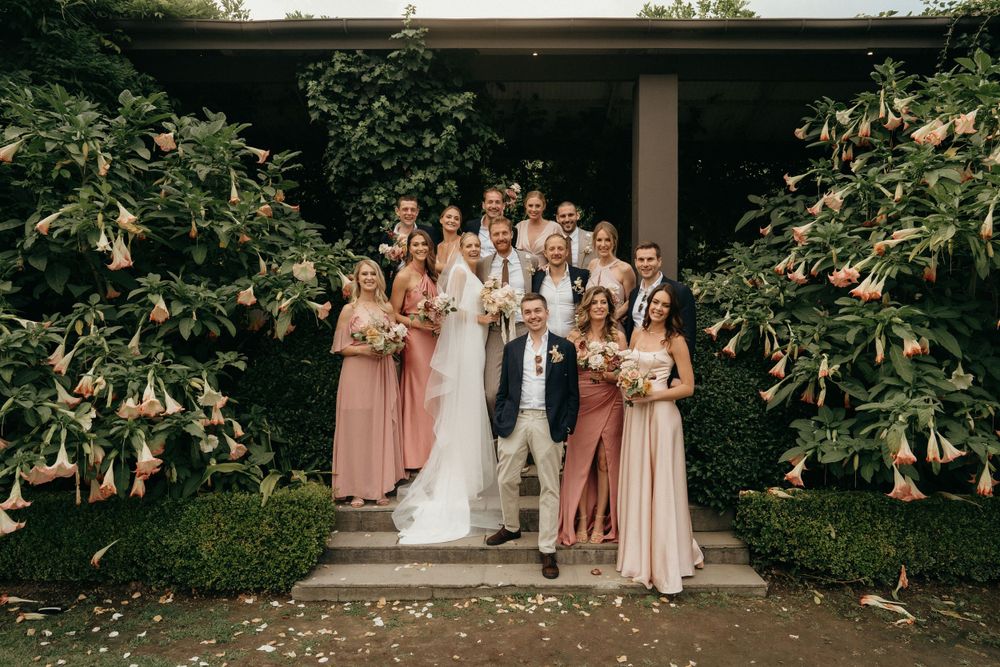 Wedding party poses on steps between blooming magnolia trees in a garden setting.