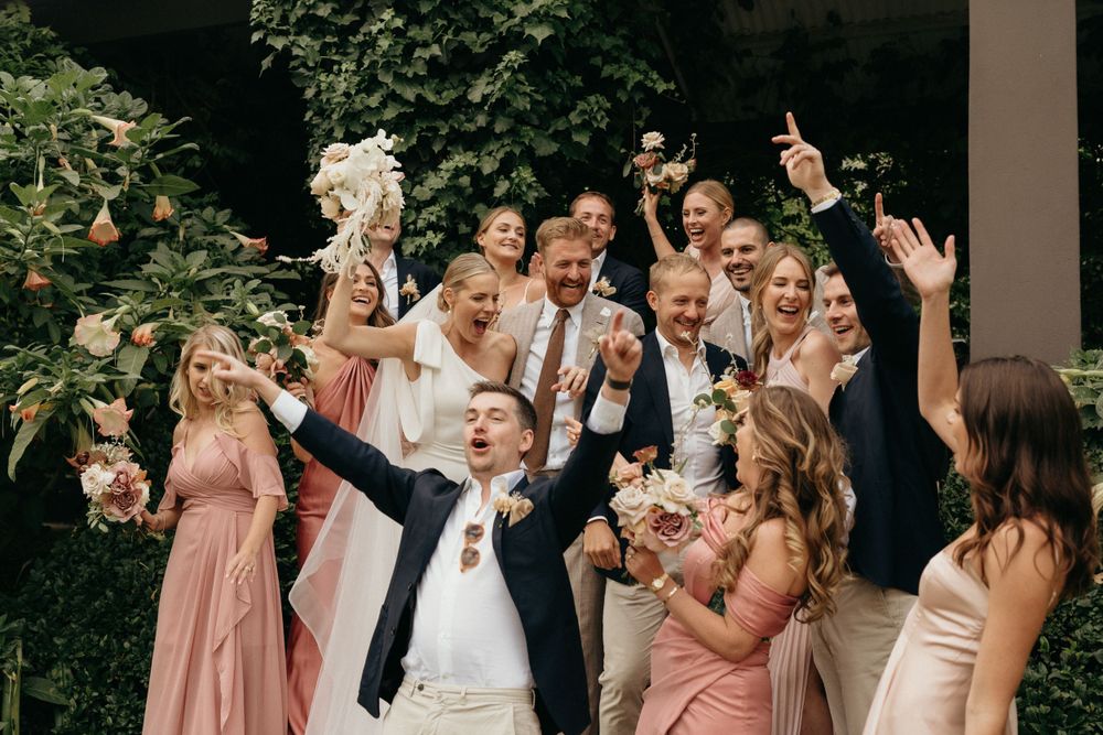 Wedding party celebrates outdoors with joyful expressions and pink bridesmaid dresses.