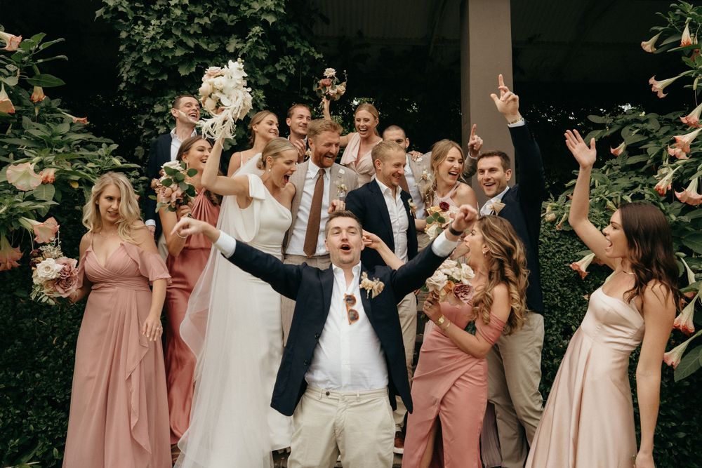 Bridal party celebrating with arms raised in joy during outdoor wedding photo session.