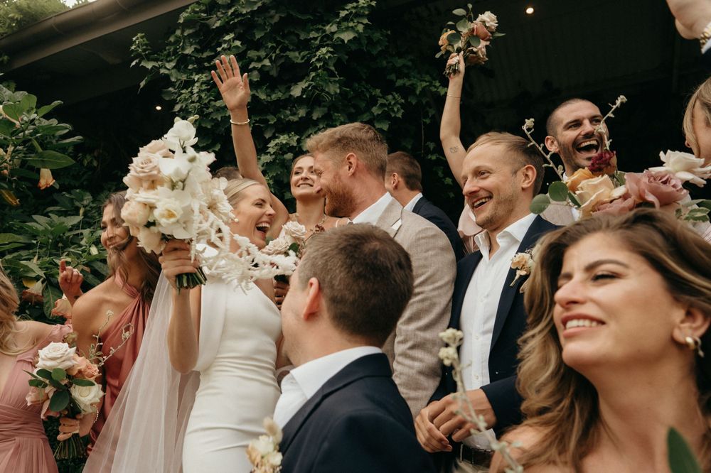 Wedding celebration outdoors with bridal party cheering amidst floral decorations.