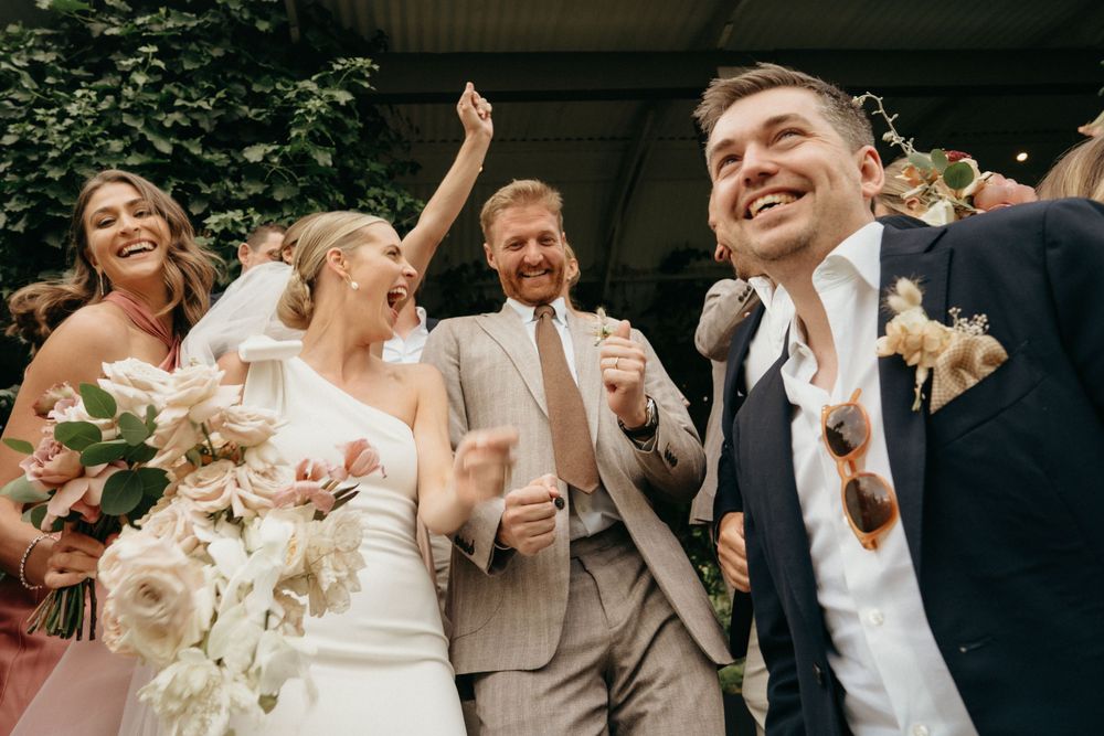 A joyous group celebrates outdoors on a sunny day with bouquets and formal attire.