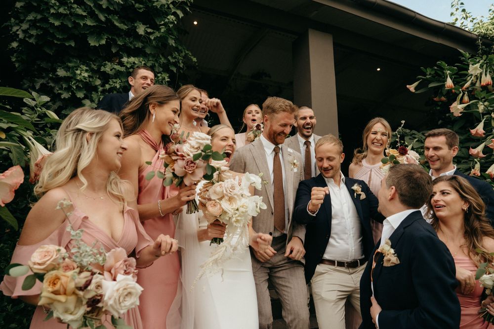 Wedding party members celebrating together outdoors in pink and neutral attire.