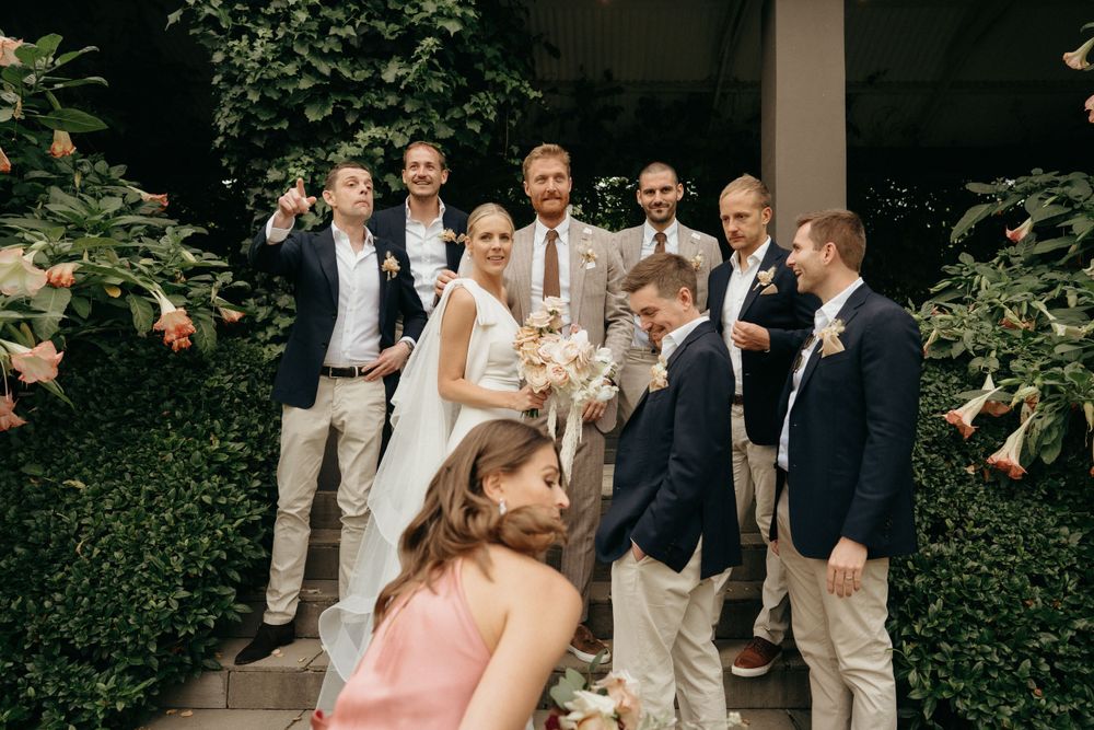Wedding party poses outdoors in elegant attire against lush garden backdrop.