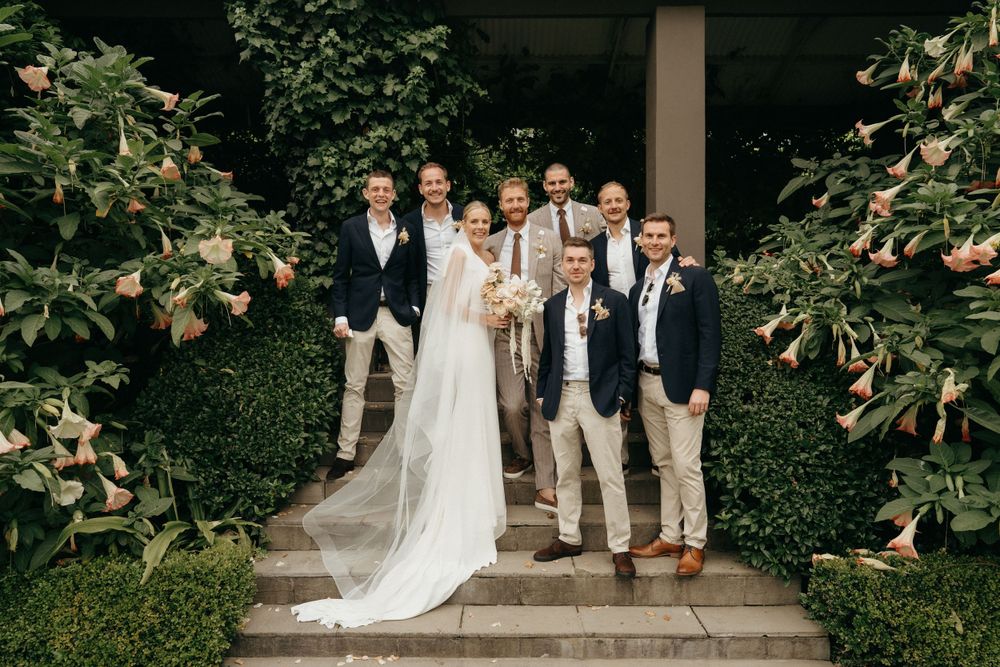 Wedding party poses on garden steps surrounded by lush greenery.