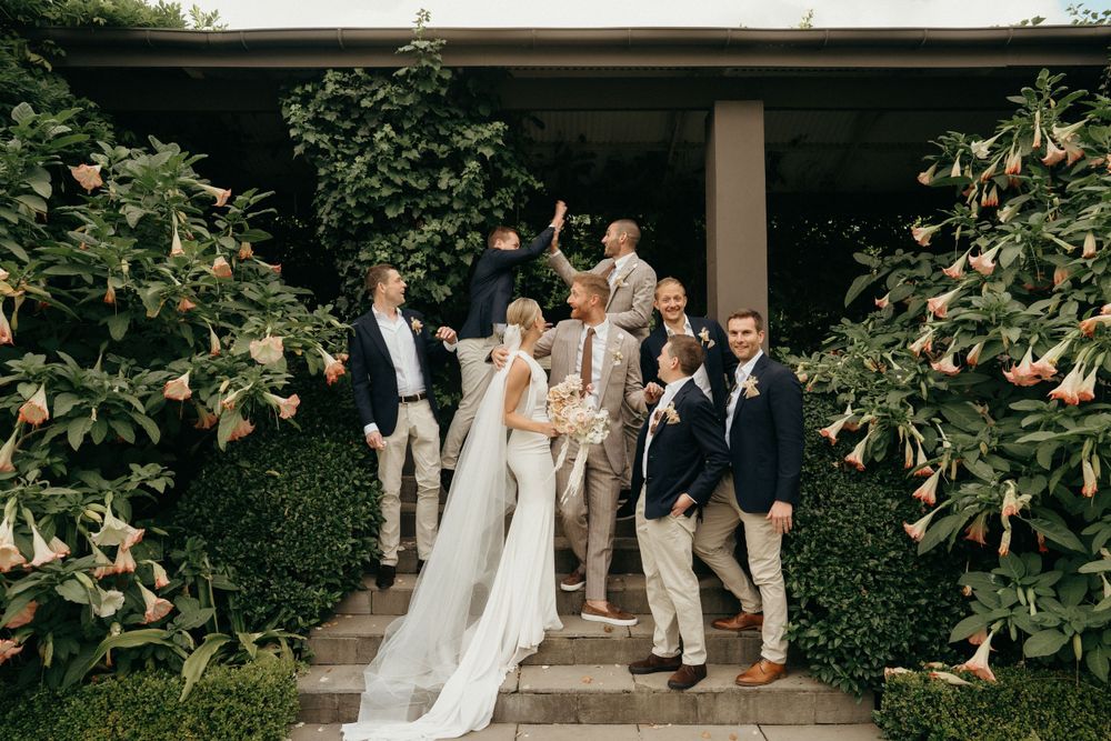 Wedding party gathered on outdoor steps surrounded by lush greenery.