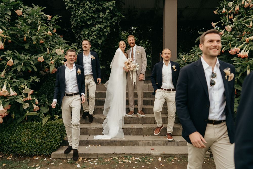 Wedding party poses on garden steps with greenery surrounding the outdoor venue.