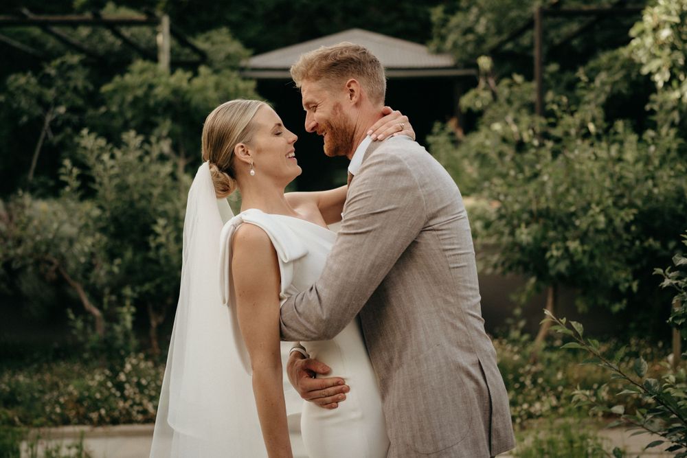Newlyweds share intimate moment in garden setting during wedding photoshoot.