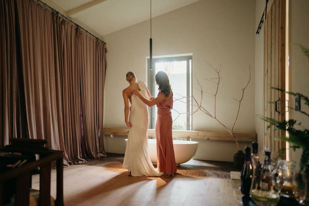 A quiet moment during wedding preparations in a sunlit room with flowing curtains.