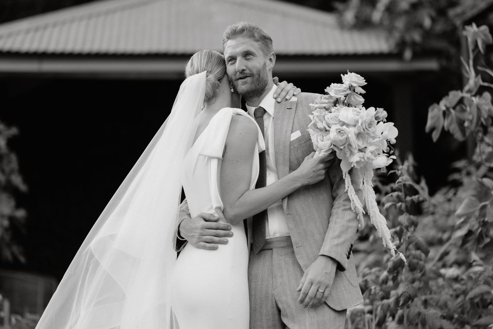 Black and white romantic portrait of newlyweds embracing outdoors with bride holding floral bouquet.