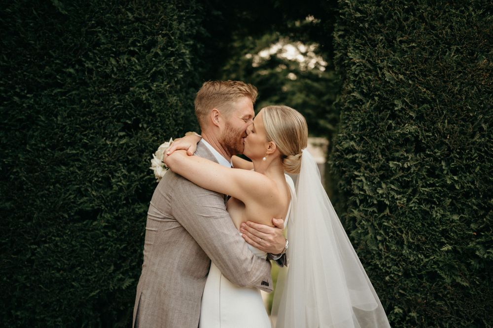Romantic moment captured between newlyweds against a lush green hedge backdrop.