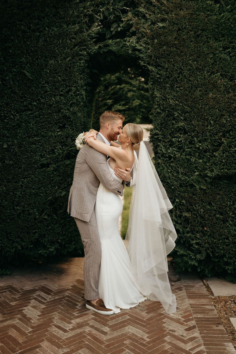 A romantic wedding moment captured against a backdrop of lush green hedges.