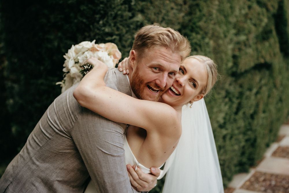 Wedding couple embraces joyfully in front of a lush garden wall.