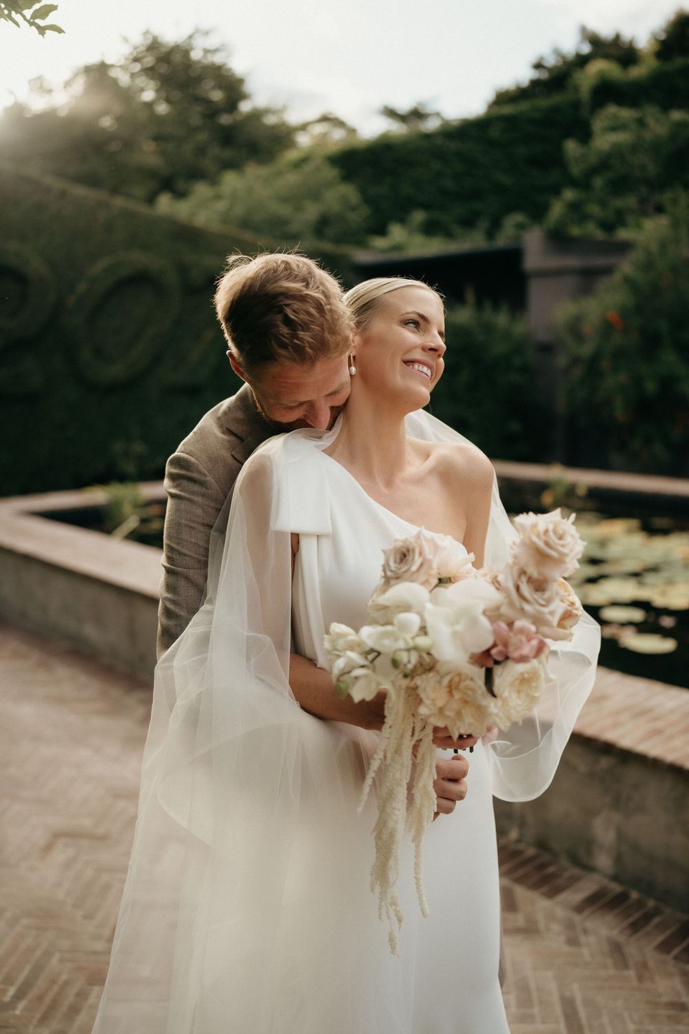 An intimate wedding photo shows a tender embrace against a garden backdrop at sunset.