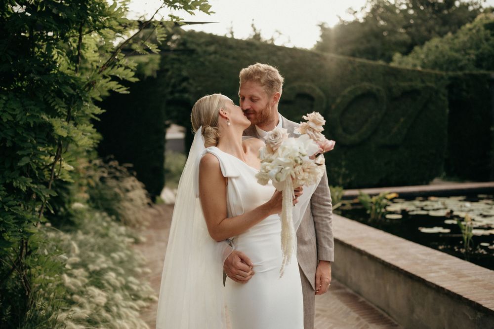 Sunset wedding portrait in garden setting with couple holding elegant white floral bouquet.