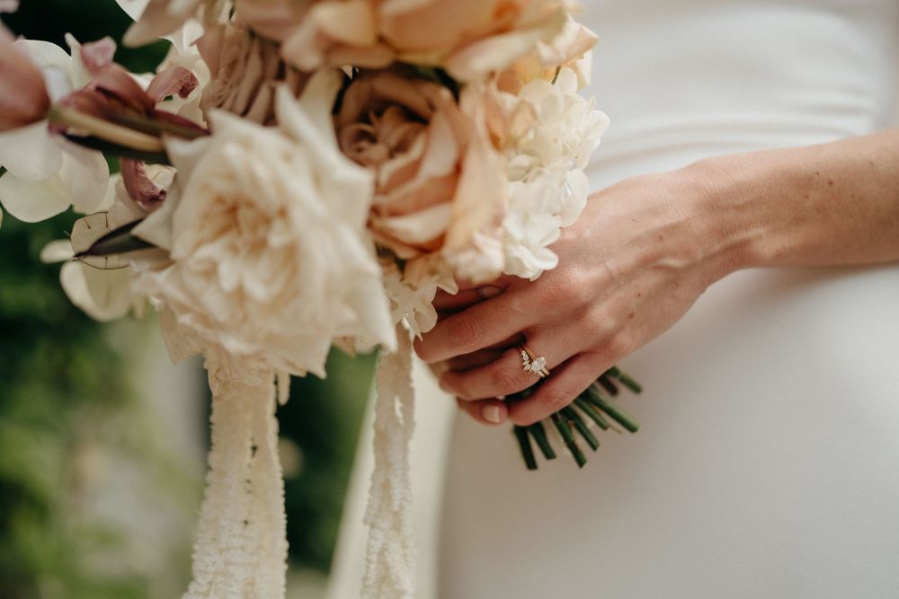A close-up shot of hands holding a delicate bouquet of blush roses wrapped in white silk ribbon.