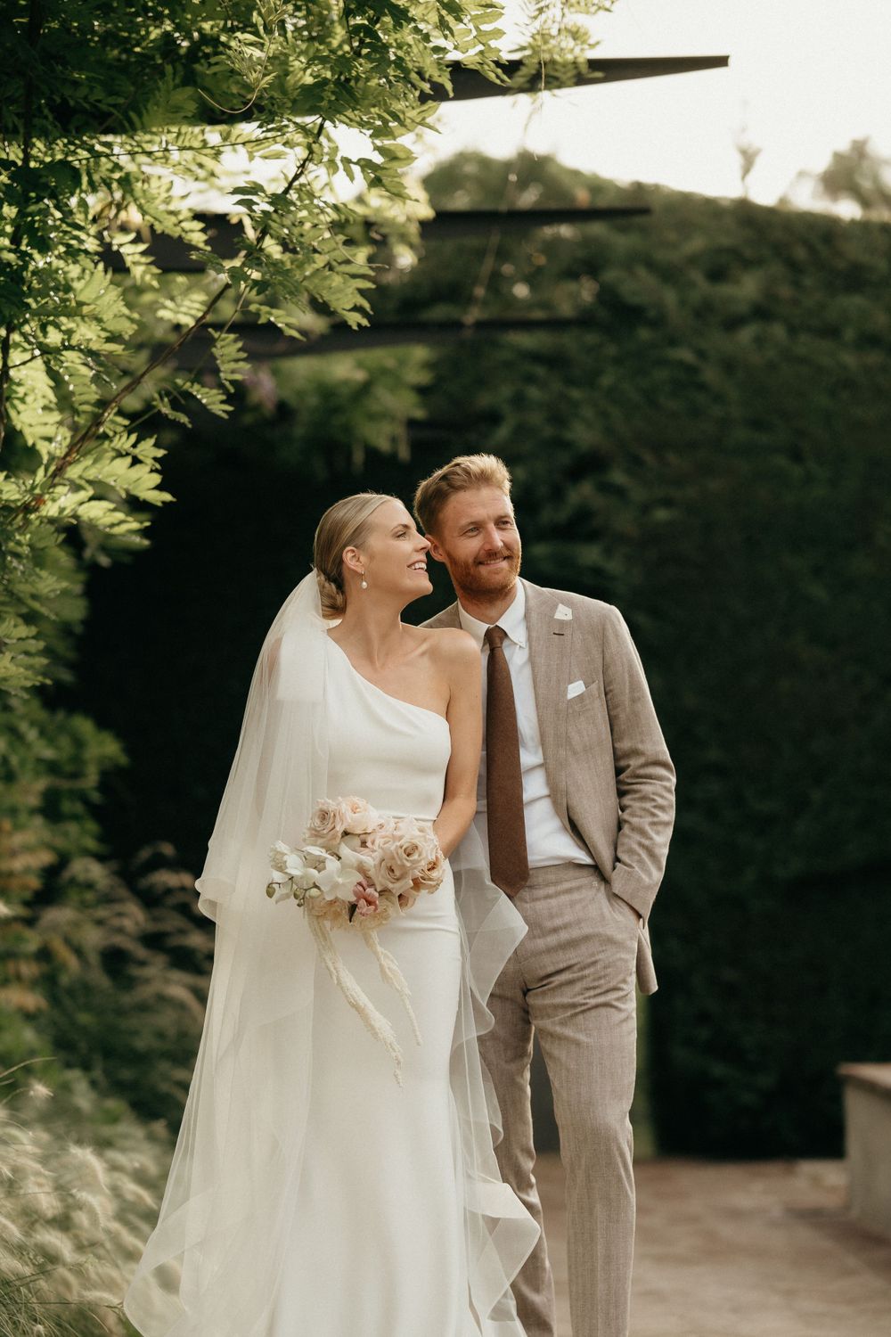 A newlywed couple poses for a romantic outdoor portrait surrounded by lush greenery.