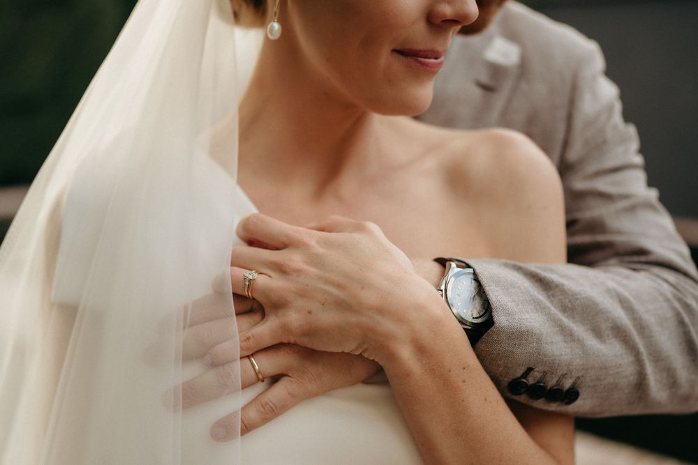 Close up detail showing elegant wedding ring and veil with grey suit in background at a wedding ceremony.
