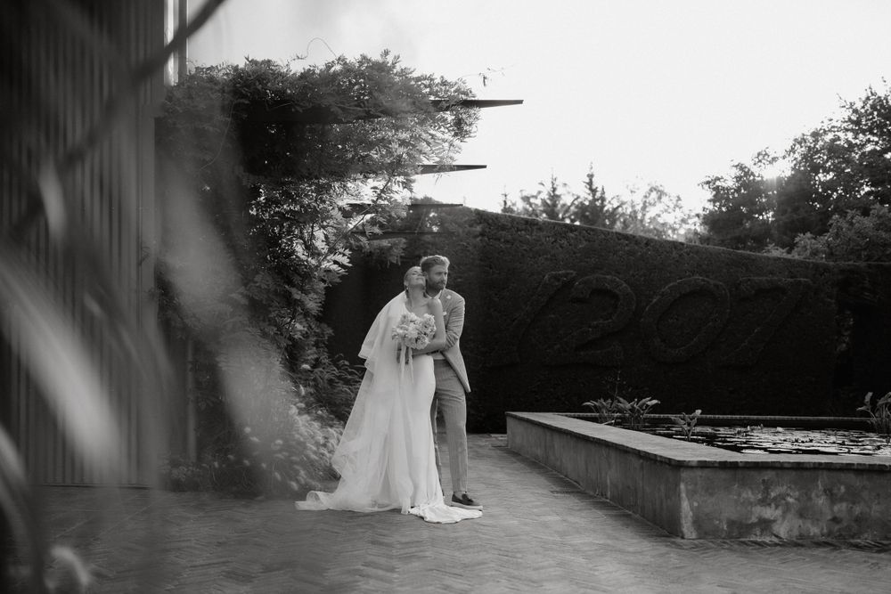 A black and white romantic moment captured in a garden setting with hedges and stone paths.