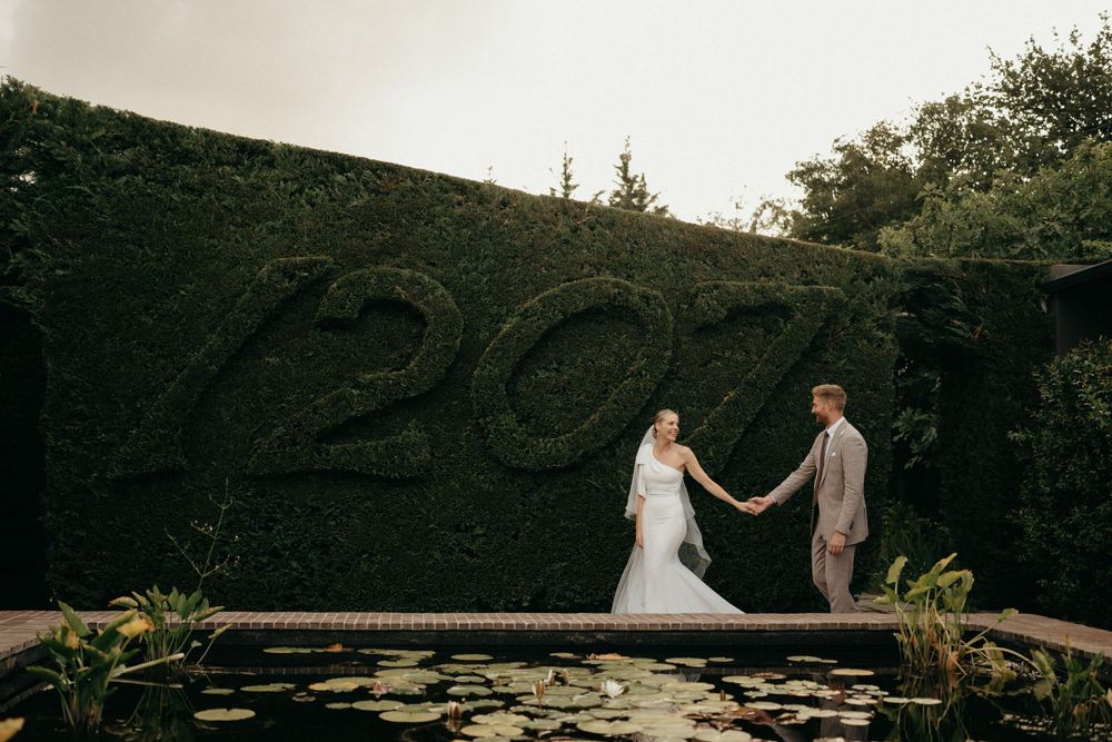 Couple poses by a reflecting pool with a hedge displaying '2020' in greenery.