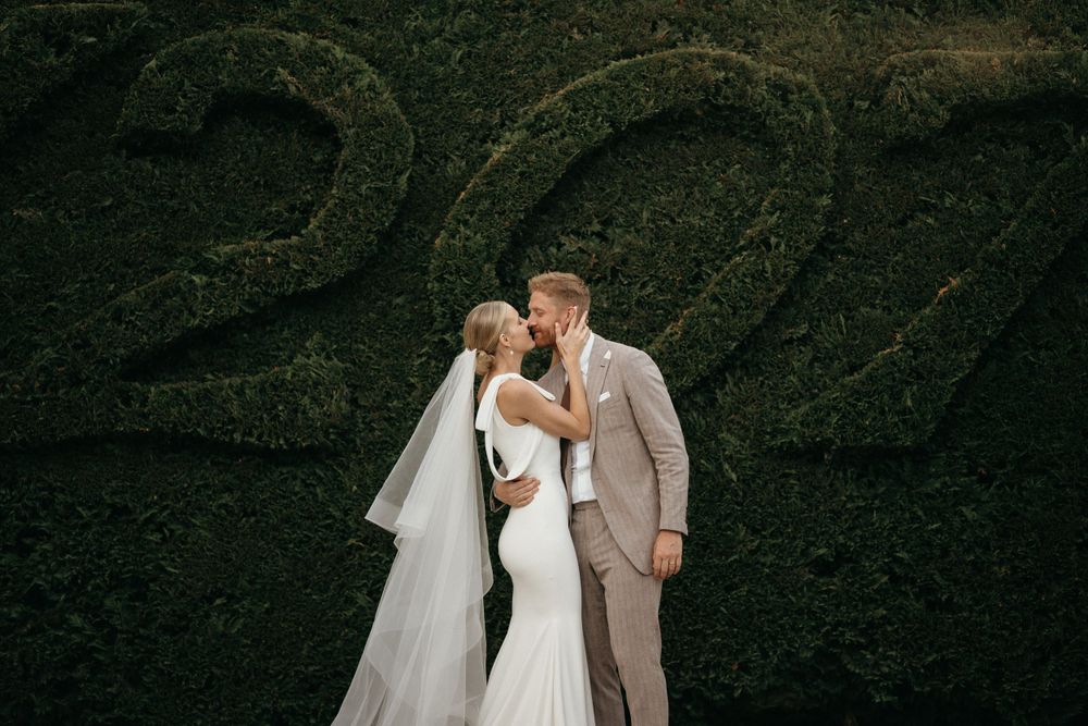 Elegant wedding couple embraces against a garden wall with number 22.