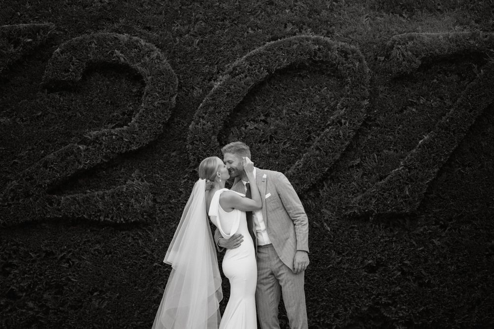 A romantic black and white wedding photo showing a couple kissing in front of a textured wall.