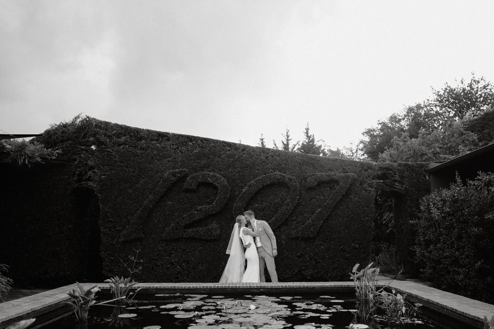 Artistic black and white wedding photo featuring silhouettes against a garden wall.