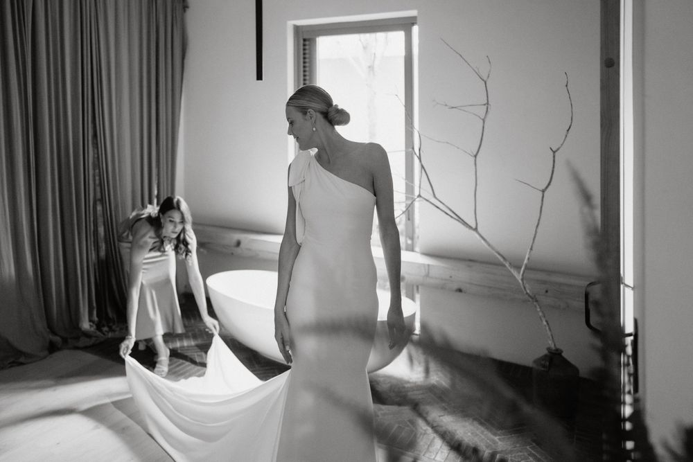 Classic black and white photograph of a bride in a one-shoulder gown with flowing train.