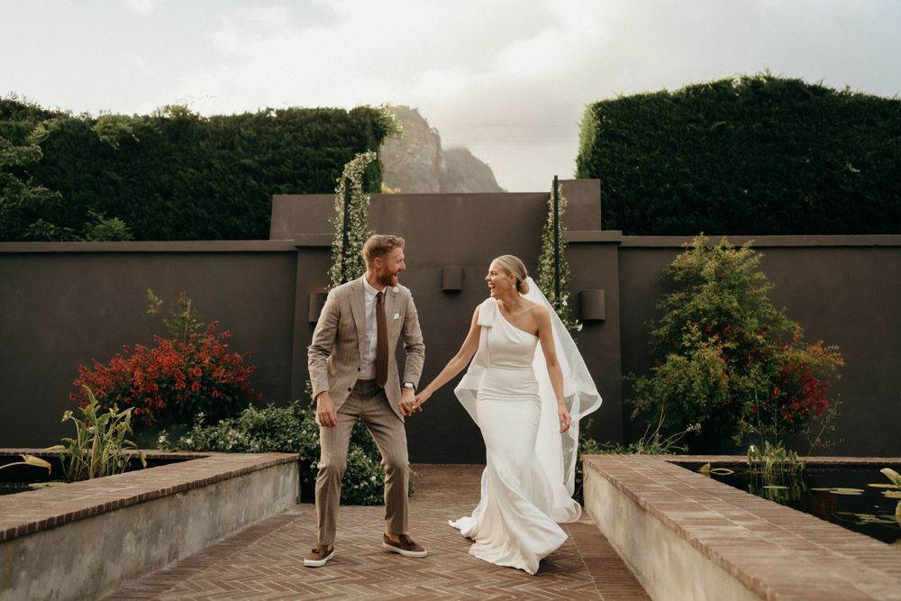 Newlyweds holding hands and walking together on stone pathway in garden setting.