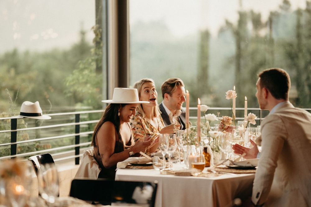 Wedding reception guests enjoy dinner and drinks on outdoor terrace at sunset.