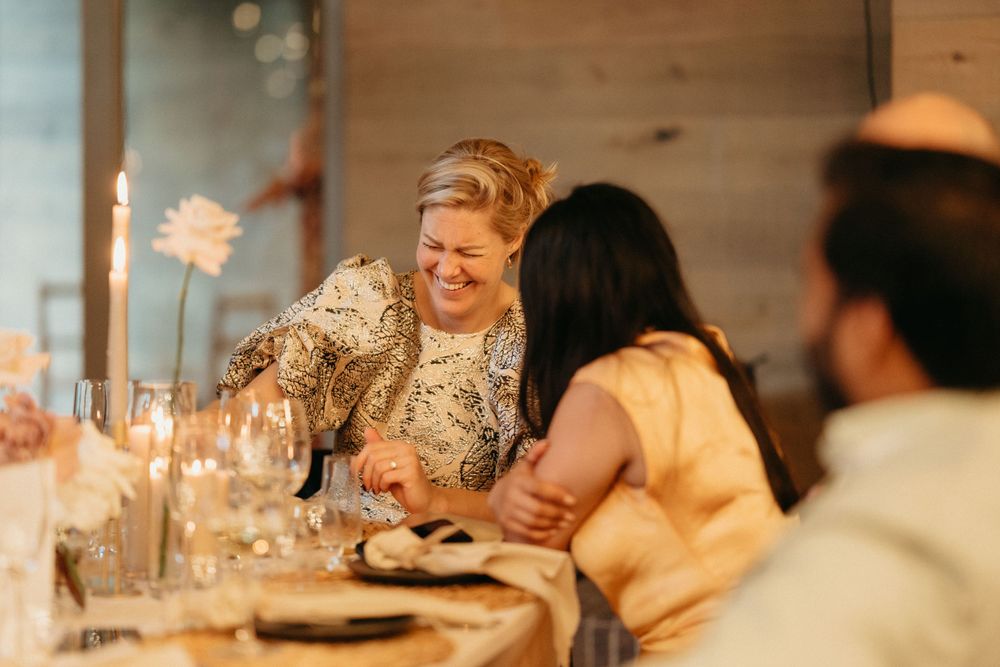 Friends enjoying a candlelit dinner party with laughter and conversation around a cozy table setting.