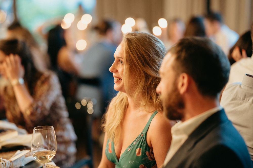 Wedding guests enjoying dinner and conversation at an evening reception with warm lighting.