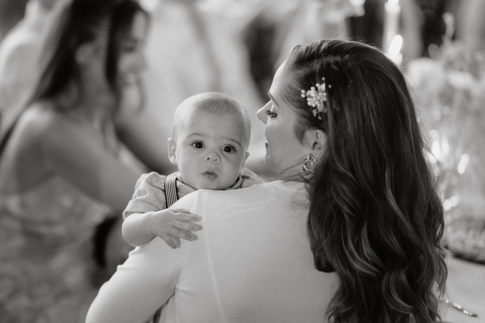 A black and white photo at a wedding captures a tender moment with a baby held during reception celebrations.