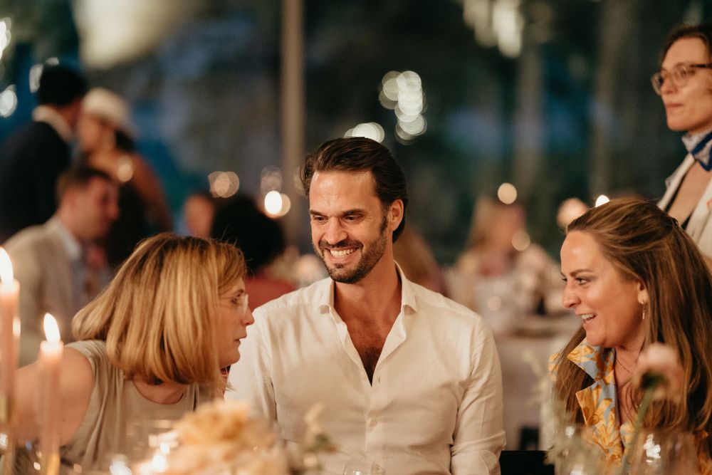 Guests sharing stories and laughter during an intimate candlelit outdoor evening gathering.