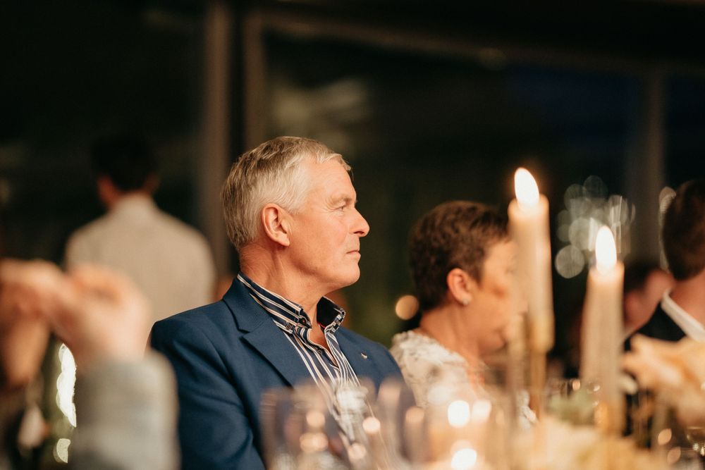 Wedding guests enjoying an intimate candlelit dinner reception under warm lighting.