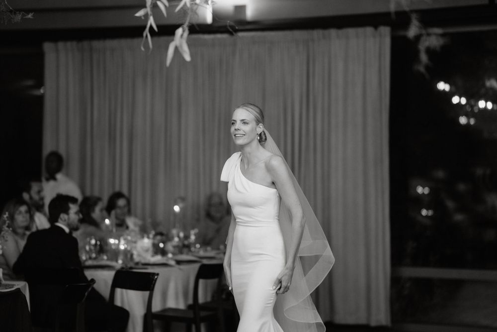 A black and white photo of a bride dancing in an elegant fitted wedding dress with flowing veil.