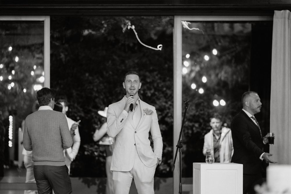 A black and white candid reception photo showing guests and celebration in an indoor-outdoor venue.